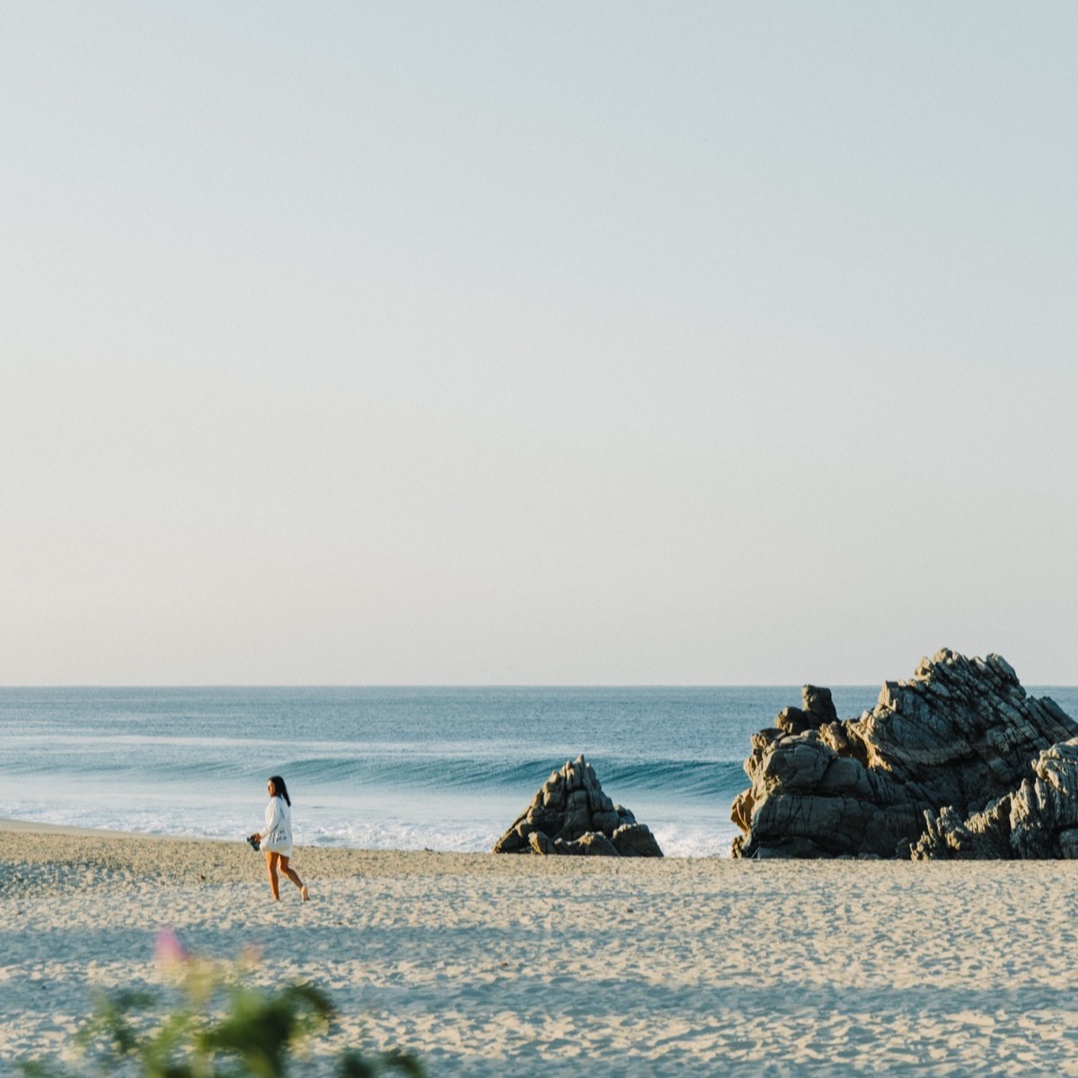 Mujer caminando por la playa de Zicatela junto a las rocas